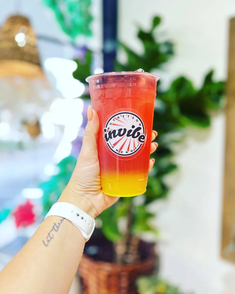 A hand holding a yellow and pink InVibe tea in daylight